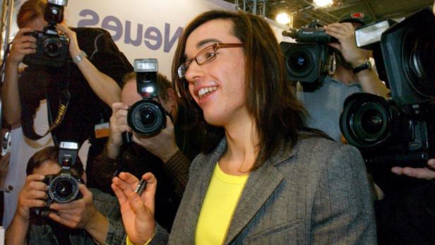 Eine Frau mit Brille lächelt, umgeben von Fotografen.