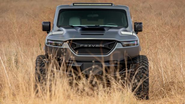 Ein grauer Rezvani Tank Offroader steht im hohen, trockenen Gras.