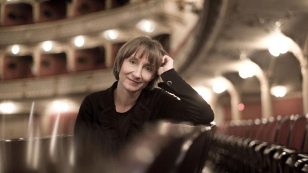 Eine Frau sitzt in einem leeren Theatersaal und lächelt.