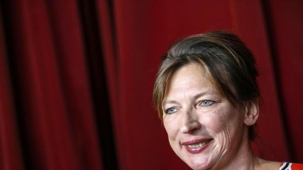 Eine Frau mit blauen Augen lächelt vor einem roten Vorhang.