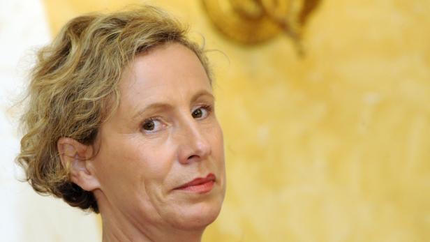 Porträt einer Frau mit blond gelocktem Haar vor einem gelben Hintergrund.