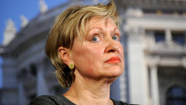 Eine Frau mit blonden Haaren und Ohrringen blickt nach oben.