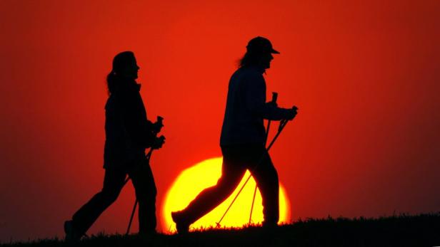 Zwei Personen machen bei Sonnenuntergang Nordic Walking.