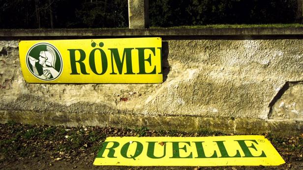 Gelbe Schilder der Marken Römer und Quelle lehnen an einer Mauer.