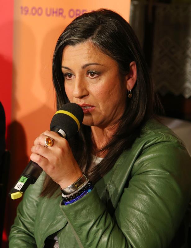 Eine Frau spricht in ein Mikrofon und trägt eine grüne Jacke.