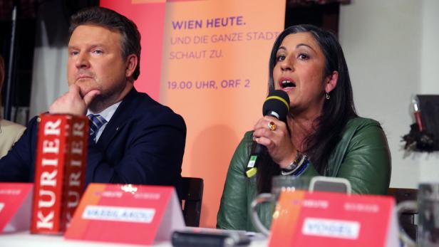 Zwei Personen sitzen an einem Tisch während einer Pressekonferenz von „Wien Heute“.