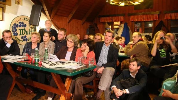 Eine Gruppe von Menschen sitzt an Tischen in einem holzgetäfelten Raum.
