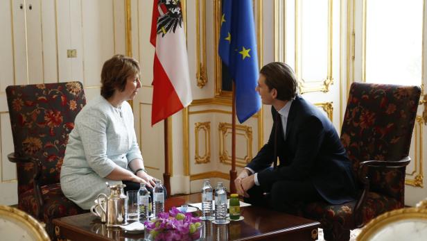 Bundespräsident Alexander Van der Bellen im Gespräch mit einer Frau vor österreichischen und EU-Flaggen.