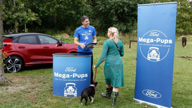 Eine Frau mit Hund spricht mit einem Mitarbeiter des „Ford Mega-Pups Pop-Up Dog Grooming Salon“.