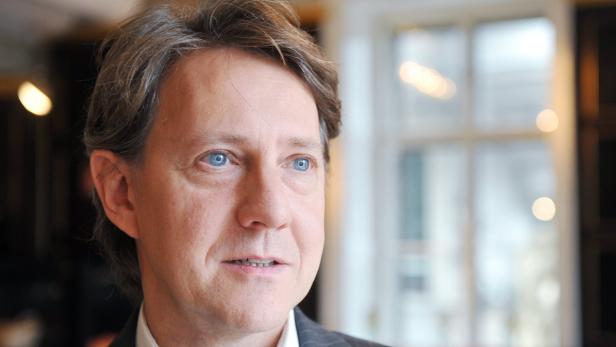 Porträt eines Mannes mit hellblauen Augen vor einem Fenster.