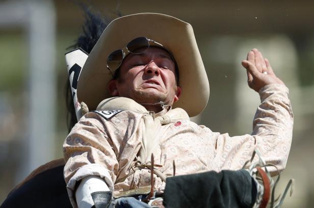 Ein Cowboy mit Sonnenbrille auf dem Hut reitet auf einem Bullen.