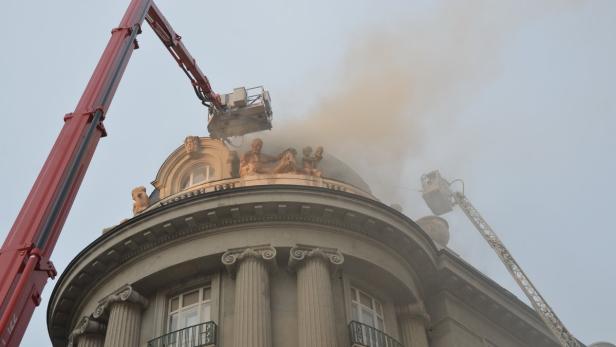 Feuerwehrleute löschen einen Brand auf dem Dach eines verzierten Gebäudes.