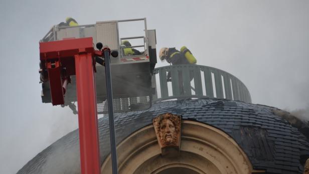 Feuerwehrleute arbeiten auf dem Dach eines Gebäudes mit einer roten Drehleiter.