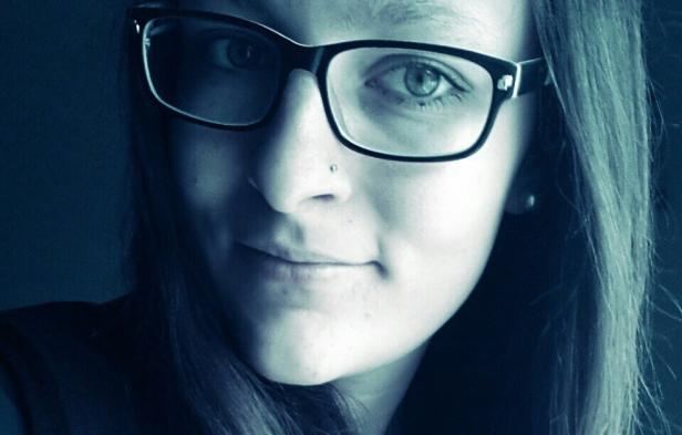 Porträt einer jungen Frau mit Brille und Nasenpiercing.