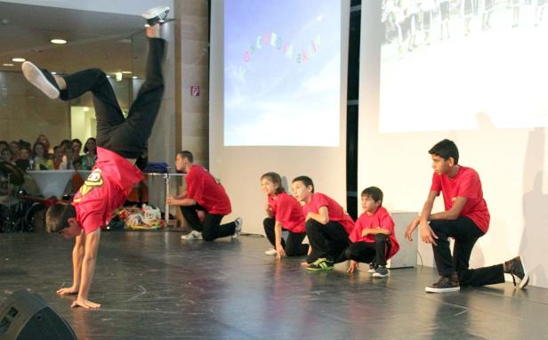 Eine Gruppe Kinder in roten T-Shirts tritt auf einer Bühne auf, ein Kind macht einen Handstand.