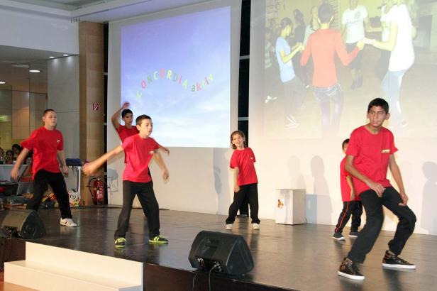Eine Gruppe Kinder in roten T-Shirts tanzt auf einer Bühne vor einer Leinwand mit der Aufschrift „Concordia aktiv“.