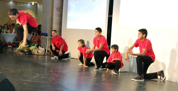 Eine Gruppe von Kindern in roten T-Shirts führt eine Tanzperformance auf einer Bühne auf.