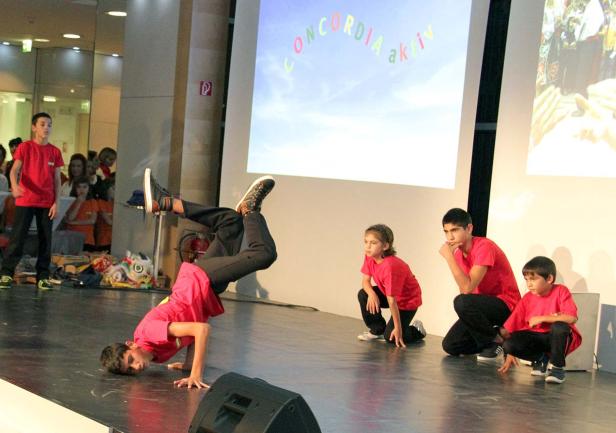 Eine Gruppe von Kindern tritt auf einer Bühne auf, ein Junge macht Breakdance.