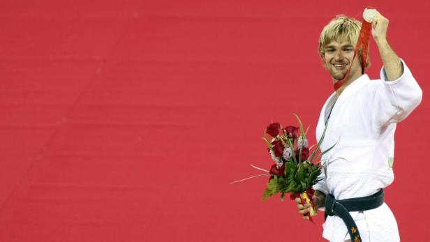 Ein Judoka mit Silbermedaille und Blumenstrauß vor rotem Hintergrund.