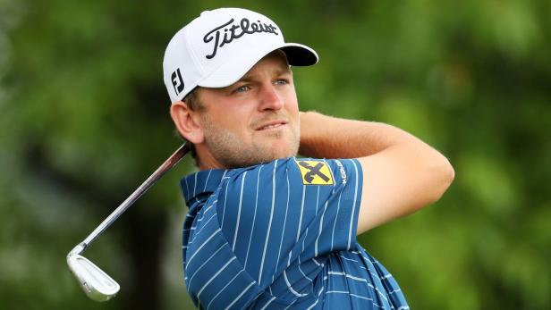 Ein Golfspieler mit blau gestreiftem Hemd und weißer Kappe beim Abschlag.