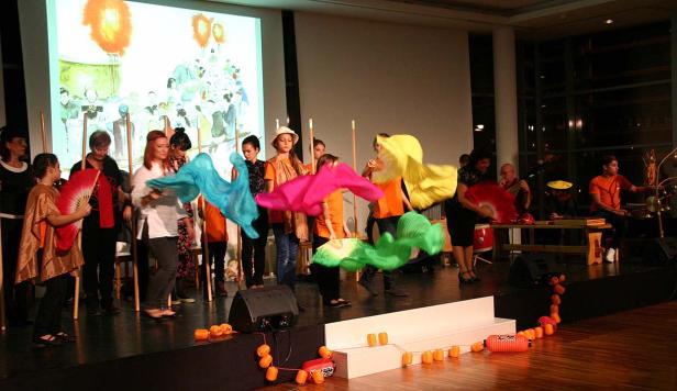 Eine Gruppe von Menschen führt eine Tanzperformance mit bunten Tüchern auf einer Bühne auf.