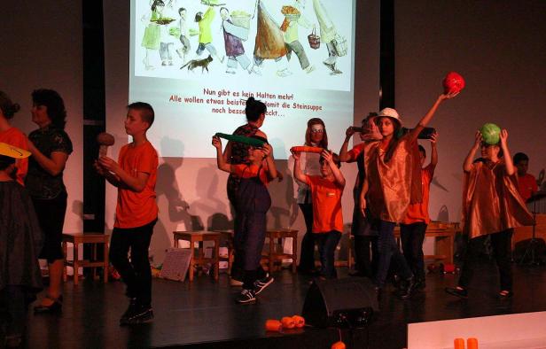 Kinder führen ein Theaterstück mit Requisiten auf einer Bühne auf.