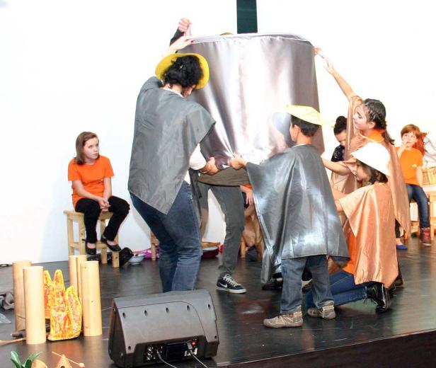 Kinder führen ein Theaterstück mit einem großen, silbernen Objekt auf einer Bühne auf.