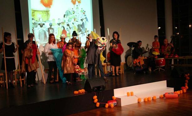Eine Gruppe von Menschen, darunter Kinder, tritt mit einer Löwenmaske auf einer Bühne auf.