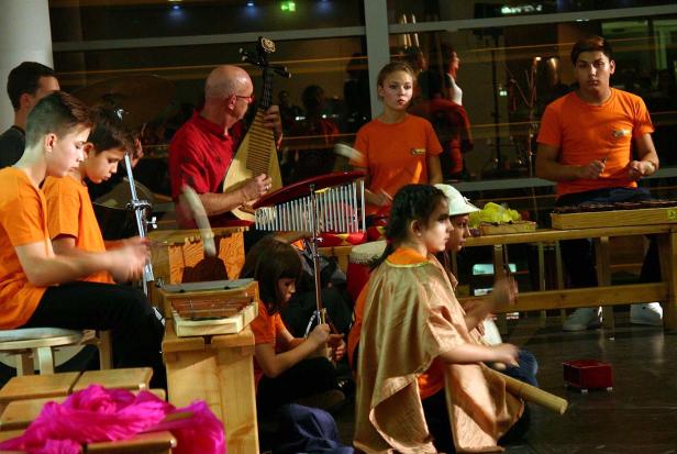 Eine Gruppe von Kindern und Erwachsenen spielt auf verschiedenen Musikinstrumenten.