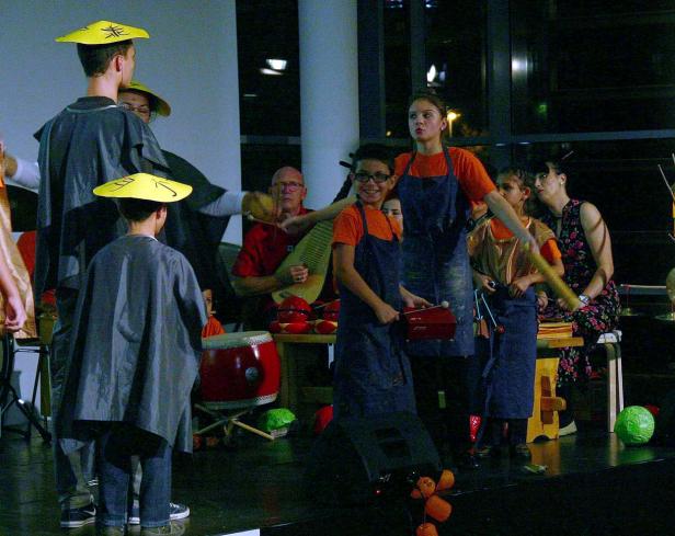 Eine Gruppe von Menschen tritt mit Musikinstrumenten und gelben Hüten auf einer Bühne auf.