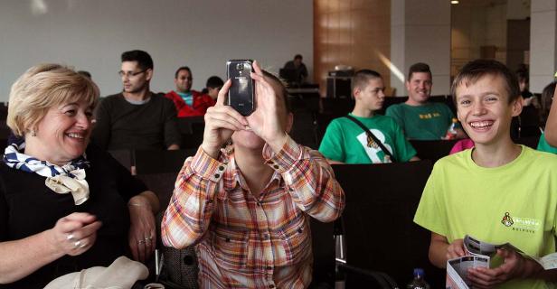 Zuschauer sitzen in einem Saal, eine Frau macht ein Foto mit ihrem Smartphone.