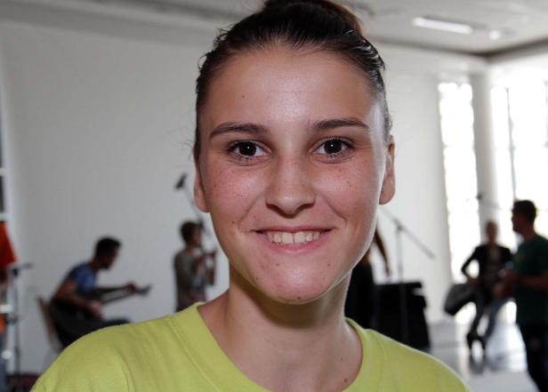 Eine lächelnde junge Frau mit Sommersprossen vor einer Band im Hintergrund.