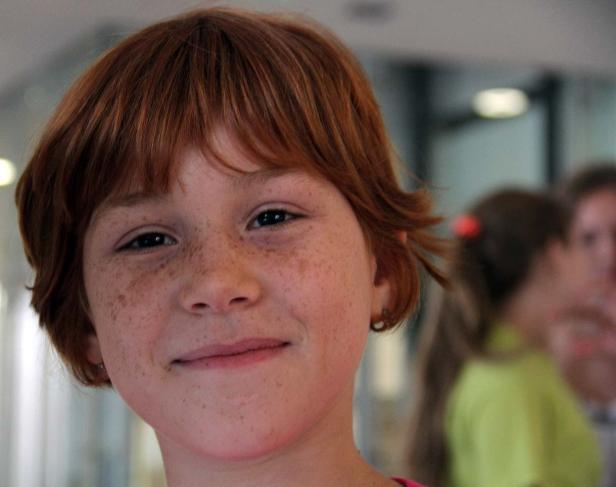 Ein lächelndes Mädchen mit roten Haaren und Sommersprossen im Gesicht.