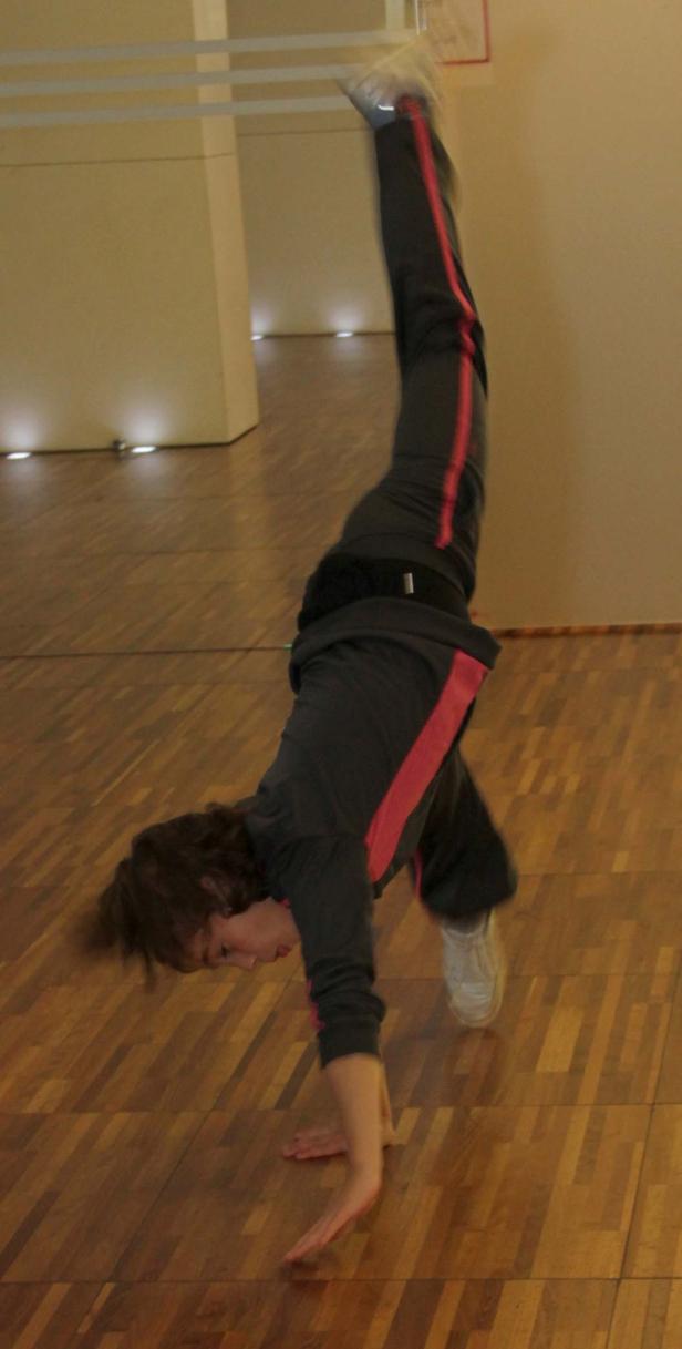 Eine Person macht einen Handstand auf einem Holzboden.