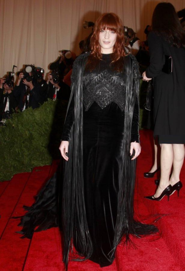Florence Welch in einem langen, schwarzen Kleid mit Fransen auf einem roten Teppich.