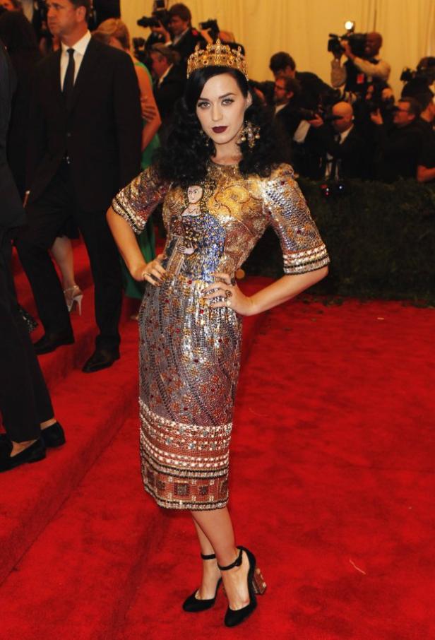 Katy Perry mit Krone und einem mit Mosaiken besetzten Kleid auf einem roten Teppich.