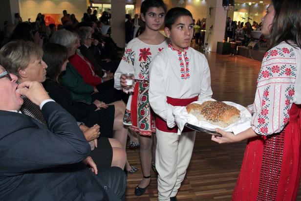 Zwei Kinder in Tracht bieten Brot und ein Glas Wasser an.