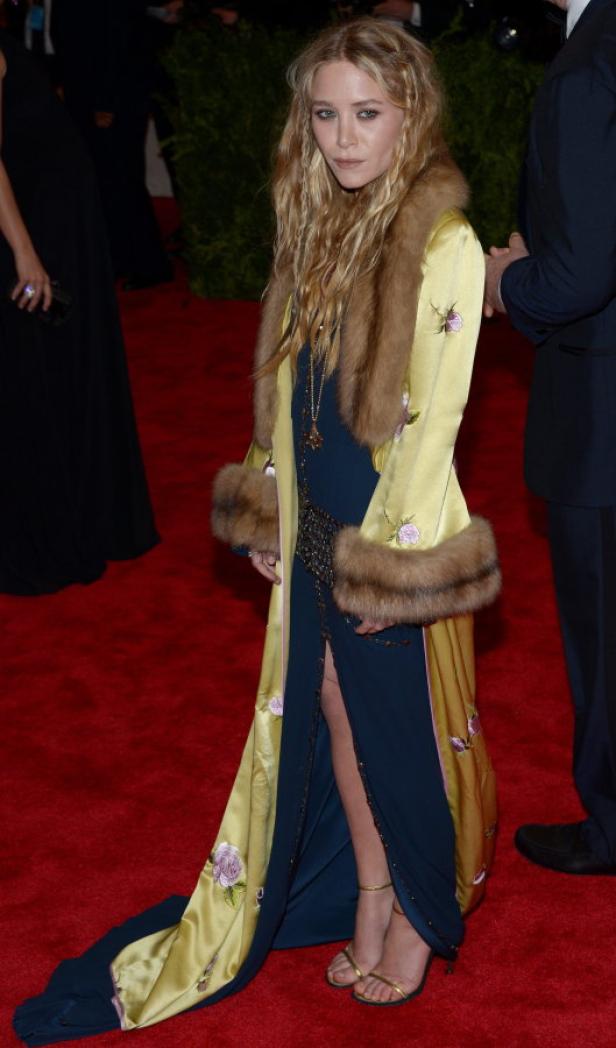 Mary-Kate Olsen in einem langen, gelben Mantel mit Pelzbesatz auf dem roten Teppich.