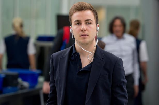 Mario Götze mit Kopfhörern und dunklem Sakko in einem öffentlichen Bereich.