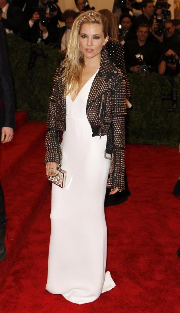 Sienna Miller trägt ein weißes Kleid und eine nietenbesetzte Jacke auf dem roten Teppich.