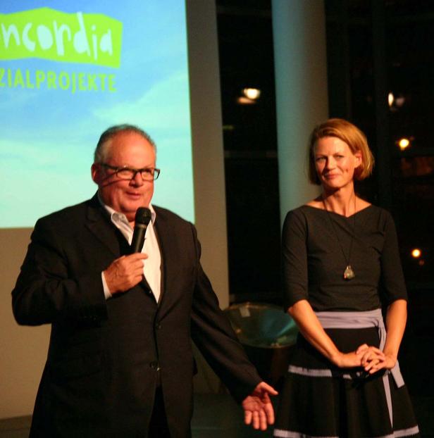 Ein Mann mit Mikrofon spricht neben einer Frau vor einer Leinwand mit der Aufschrift „Concordia“.