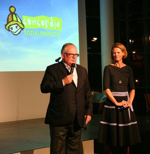 Ein Mann spricht am Mikrofon, während eine Frau daneben steht; im Hintergrund das Logo von Concordia Sozialprojekte.