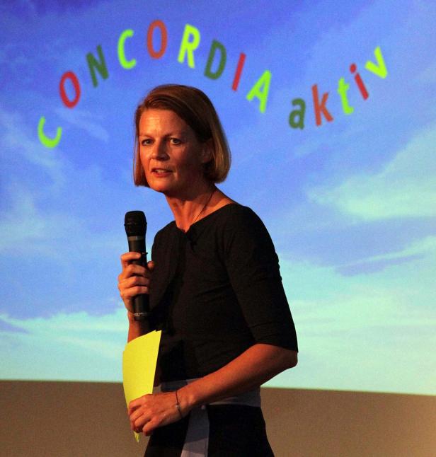 Eine Frau spricht bei einer Veranstaltung vor einem Bildschirm mit der Aufschrift „Concordia aktiv“.