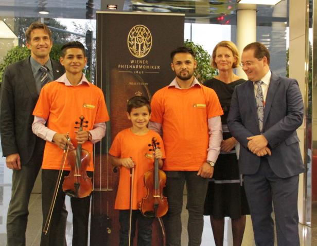 Eine Gruppe von Menschen, darunter Kinder mit Geigen, posiert vor einem Banner der Wiener Philharmoniker.