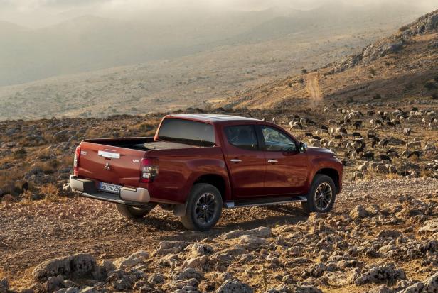 Ein roter Mitsubishi L200 Pickup steht in einer hügeligen Landschaft mit einer Schafherde.