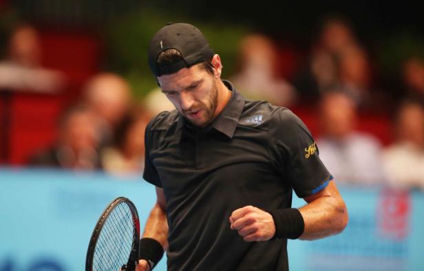 Ein Tennisspieler mit schwarzer Kappe und schwarzem Hemd auf dem Platz.