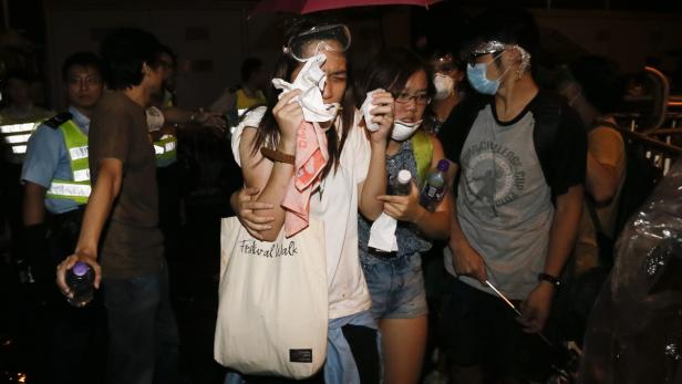 Mehrere Demonstranten schützen sich vor Tränengas in einer dunklen Straße.