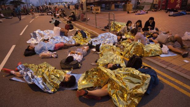 Menschen schlafen auf der Straße, in goldene Rettungsdecken gehüllt.