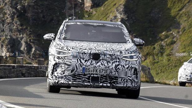 Ein mit Tarnmuster beklebter VW ID.4 auf einer Bergstraße.