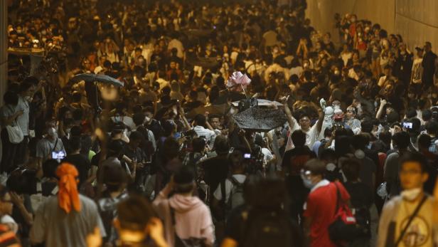Eine große Menschenmenge demonstriert mit erhobenen Händen und Regenschirmen.